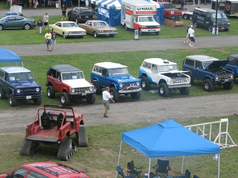 Row of lifted early Ford Broncos at a show, with a red track-converted Bronco in front