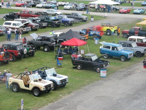 1992 Ford Bronco - A tan Ford Bronco convertible is parked on the grass at an outdoor car show, with other Broncos and vehicles visible.