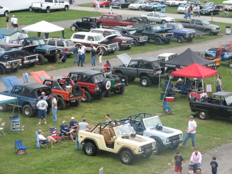 1992 Ford Bronco - A collection of classic Ford Broncos are displayed on a grassy field, with attendees gathered around.