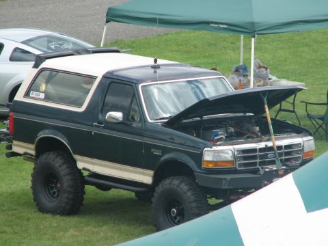 1992 Ford Bronco - A lifted 1992 Ford Bronco with its hood open is parked on grass next to another vehicle.
