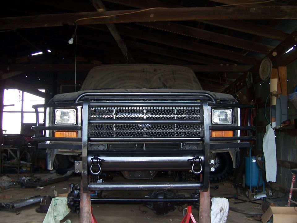 Front view of a 1983 Ford Bronco in a garage, covered in dust, with a large brush guard installed