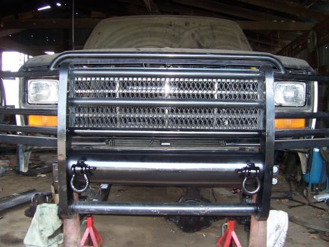1983 Ford Bronco - A dusty 1980s Ford Bronco is parked indoors, fitted with a heavy-duty brush guard and tow hooks.