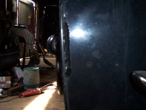 1983 Ford Bronco - Close-up of a dark-colored vehicle door, showing wear and tear in a cluttered workshop environment.