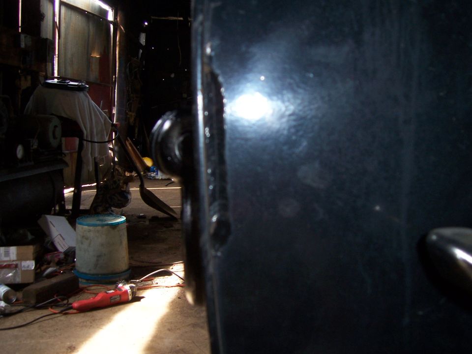 Black vehicle door with visible damage, parked in a dimly lit garage with tools and supplies nearby