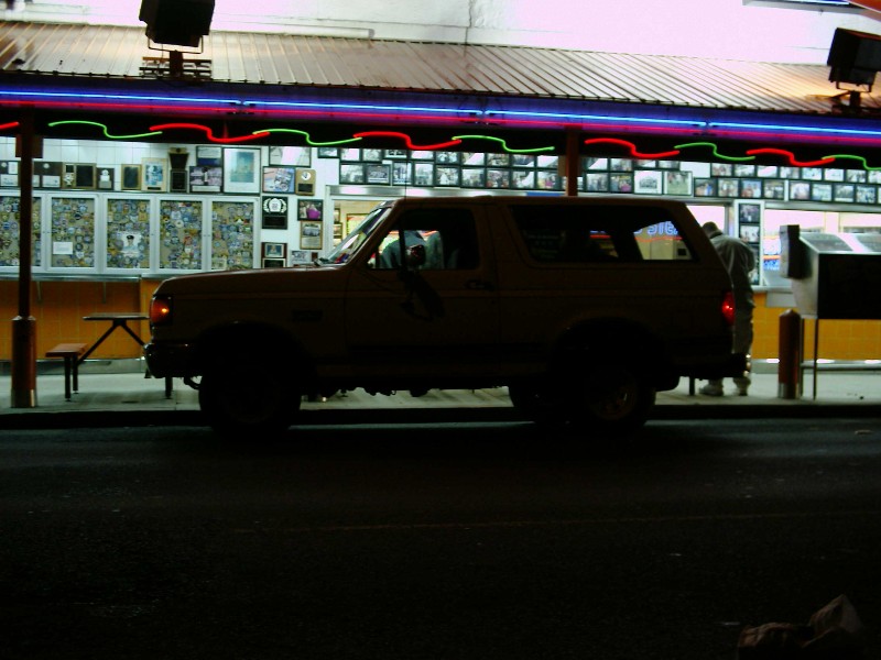 Side view of a 1987 Ford Bronco parked in front of a diner at night
