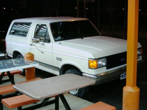 1988 Ford Bronco - A white Ford Bronco is parked near outdoor picnic tables at night.