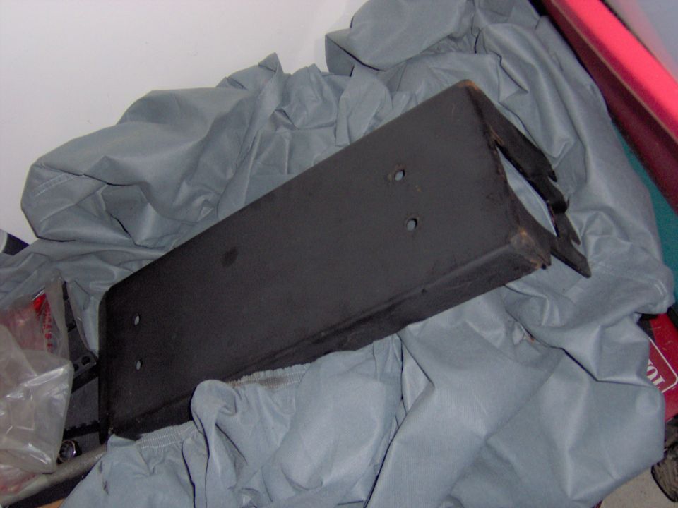 Black steel bracket with drilled bolt holes resting on a gray car cover