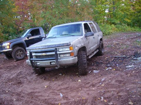 2000 Chevrolet Tahoe - Two trucks are parked in a muddy area with trees in the background.