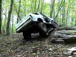 1995 Ford Bronco - A white SUV navigates a rocky incline in a forest setting, with a SuperMotors logo visible at the bottom.