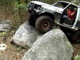 1995 Ford Bronco - A white Ford Bronco navigates a rocky trail with its door open and front end damaged.