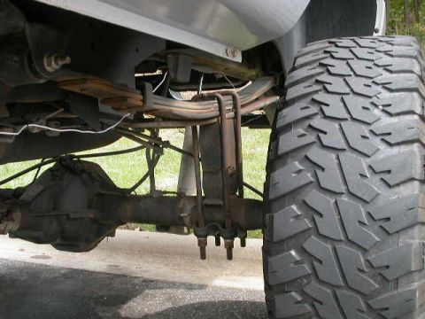 1990 Ford Bronco - Close-up view of a truck's rear axle, suspension, and tire.