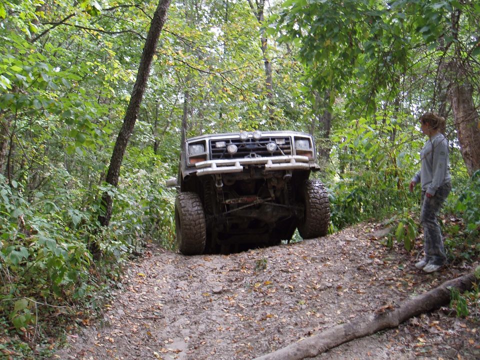 Ford Bronco tilted on a muddy trail, front view. Off-road tires, aftermarket bumper with lights
