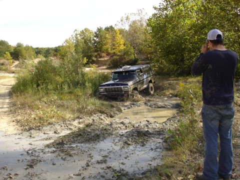 1979 Ford Bronco - A 1979 Ford Bronco navigates a muddy off-road trail, with a person observing from the side.