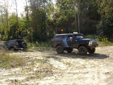1979 Ford Bronco - Two Ford Broncos navigate a muddy off-road course with trees in the background.