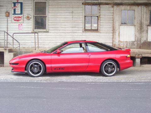 1997 Ford Probe - A red 1997 Ford Probe GTS is seen from the side, parked in front of an old wooden building.