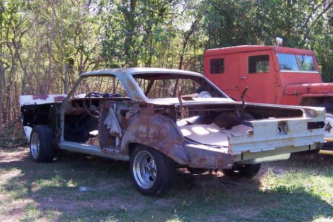 1964 Mercury Comet - This heavily rusted 1964 Mercury Comet is missing many parts and sits next to a red truck in an outdoor setting.