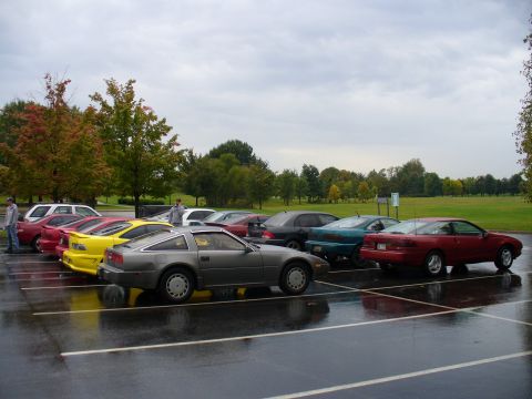 1991 Ford Probe - Several cars are parked in a wet lot under an overcast sky, with trees in the background.