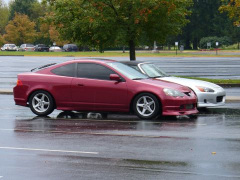 1991 Ford Probe - Two sports cars, a red coupe and a silver convertible, are parked side-by-side in a wet parking lot.