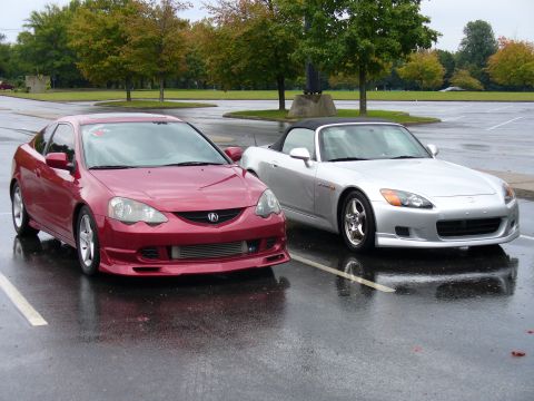 1991 Ford Probe - Two sporty coupes, a red Acura and a silver Honda, sit side-by-side in a parking lot after a rain shower.