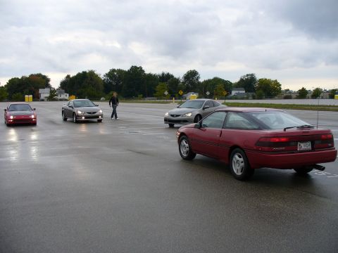 1991 Ford Probe - A red 1991 Ford Probe is parked on a wet asphalt lot with other cars and a person walking.
