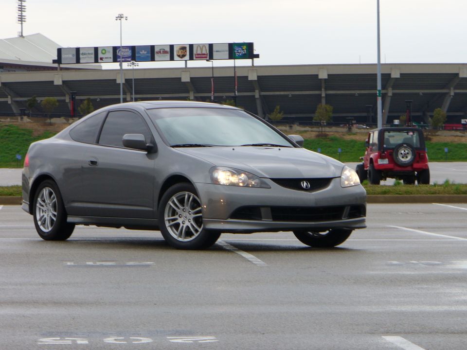 Gray coupe, 3/4 front view, with a red Jeep in the background