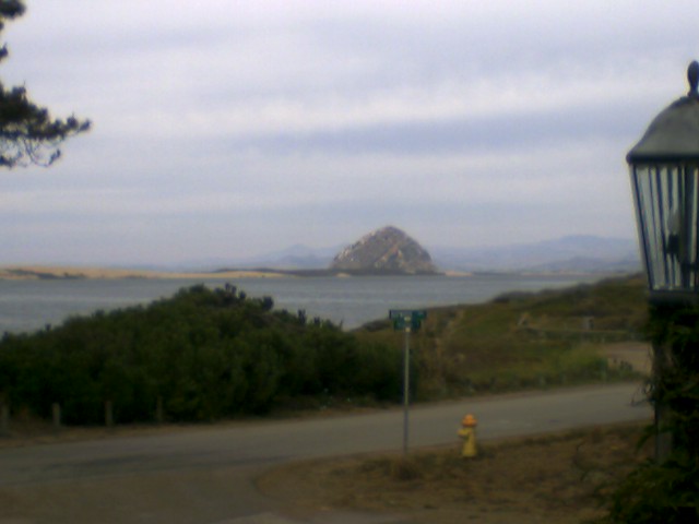 Overcast coastal view of Morro Rock across the bay with roadway and hydrant in foreground