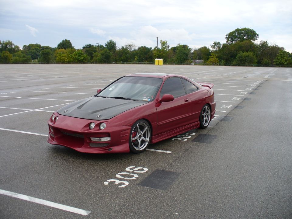 Red coupe with aftermarket carbon fiber hood and spoiler parked in a lot