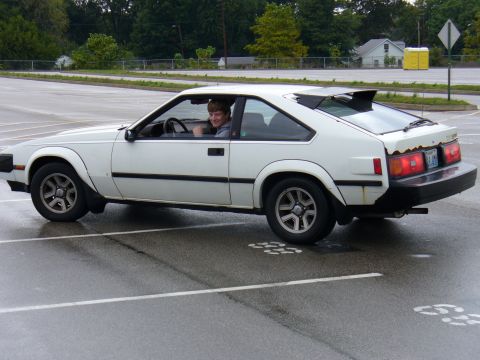 1991 Ford Probe - A person drives a white coupe in a parking lot on a wet day.