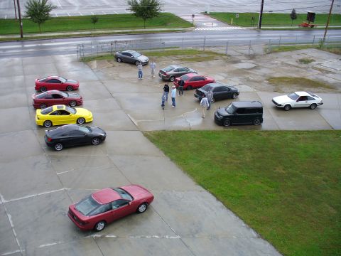 1991 Ford Probe - A collection of vehicles and people gathered in an outdoor lot.
