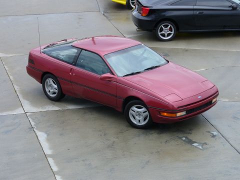 1991 Ford Probe - A red 1991 Ford Probe is parked on a concrete surface next to another vehicle.