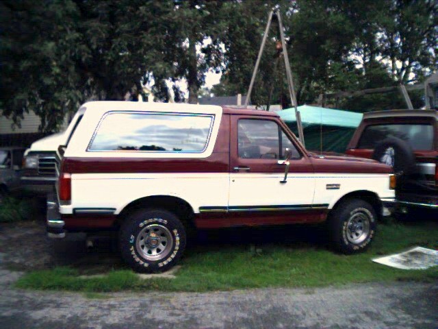 Burgundy and cream Ford Bronco SUV parked in side view on grass