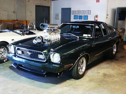 2001 Mercury Grand Marquis - Customized 1975 Ford Mustang with a prominent supercharger, parked indoors next to another vehicle.