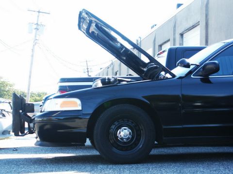 2001 Mercury Grand Marquis - A black sedan with its hood open is parked next to a pickup truck, revealing its engine compartment.
