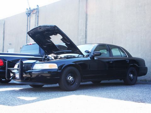 2001 Mercury Grand Marquis - A black sedan, possibly a Ford Crown Victoria, is parked with its hood open next to a pickup truck.