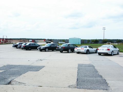 2001 Mercury Grand Marquis - A line of cars, including a white Corvette and a silver Pontiac GTO, are parked in an outdoor lot under a cloudy sky.