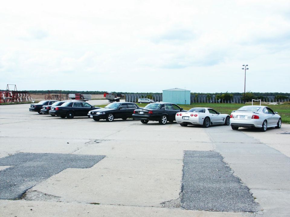 Several cars parked on asphalt, including a white Corvette and a silver Pontiac GTO
