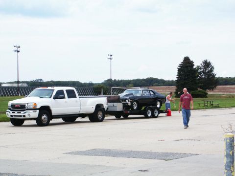 2001 Mercury Grand Marquis - White GMC pickup truck transports a black muscle car on a trailer, with two people nearby.