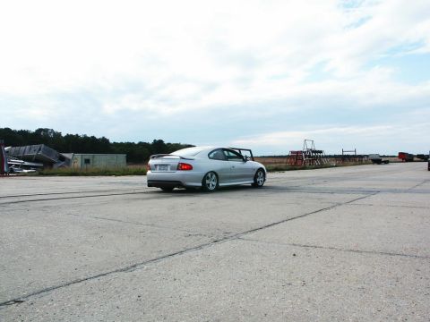 2001 Mercury Grand Marquis - Silver 2004 Pontiac GTO captured from the rear as it drives on a concrete surface, with industrial debris in the background.
