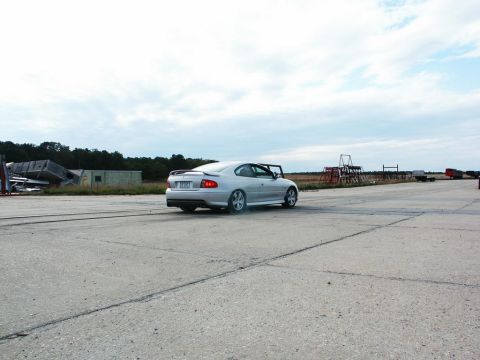 2001 Mercury Grand Marquis - Silver coupe with spoiler driving on asphalt, trees and structures in background.
