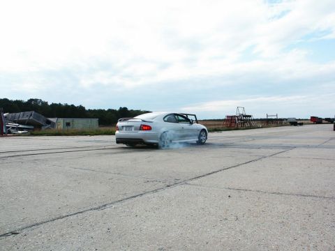 2001 Mercury Grand Marquis - A silver coupe performs a burnout, kicking up smoke from its rear tires on a paved surface under a cloudy sky.