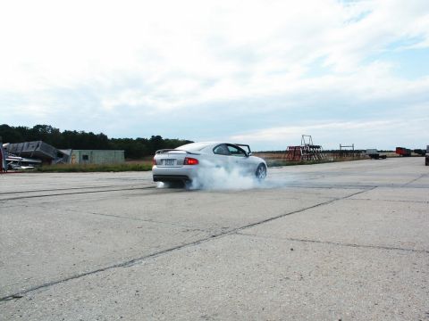 2001 Mercury Grand Marquis - A silver coupe performs a burnout on a paved surface, kicking up a cloud of smoke.