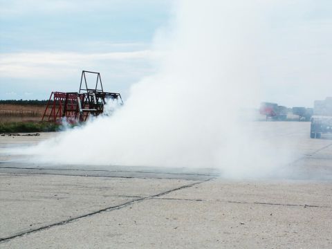 2001 Mercury Grand Marquis - Smoke obscures a metal structure on a paved area, with trucks visible in the distance.