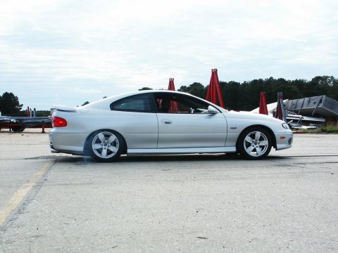2001 Mercury Grand Marquis - Silver coupe with a spoiler is seen from the side, kicking up smoke from its rear tire on a paved surface.