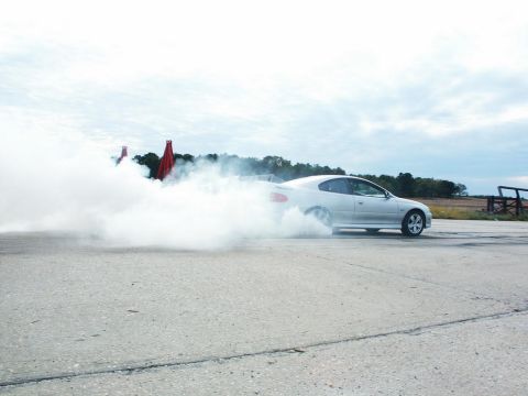 2001 Mercury Grand Marquis - A silver coupe performs a burnout, generating a large cloud of smoke against a cloudy sky.