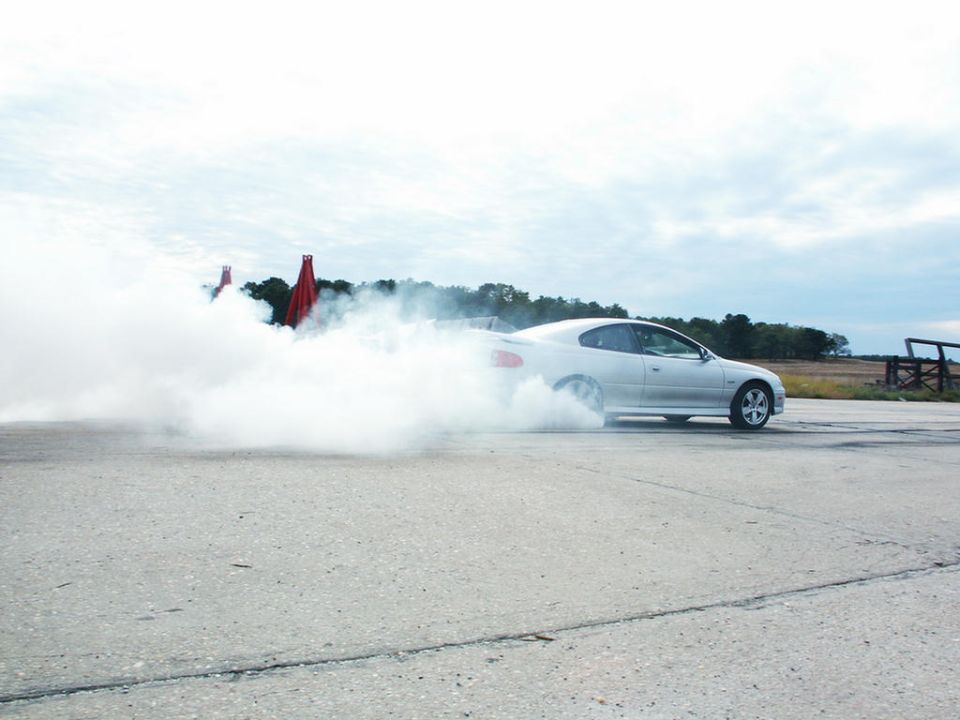 Silver coupe doing a burnout, kicking up a lot of smoke. Red cones visible in the background