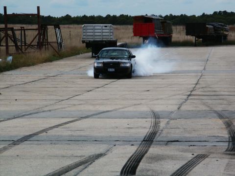 2001 Mercury Grand Marquis - A black sedan drifts, creating a large cloud of smoke on a concrete surface with visible tire tracks.
