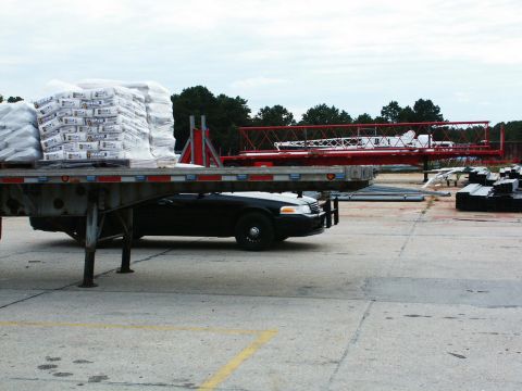2001 Mercury Grand Marquis - A black sedan is being transported on a flatbed trailer, alongside construction materials and crane components.