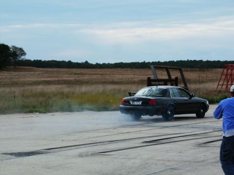 2001 Mercury Grand Marquis - A black 2001 Mercury Grand Marquis performs a burnout, kicking up smoke on a track with a field in the background.