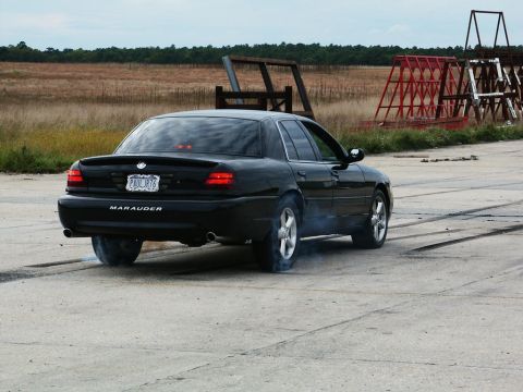 2001 Mercury Grand Marquis - Black sedan performing a burnout on a paved surface with a field in the background.