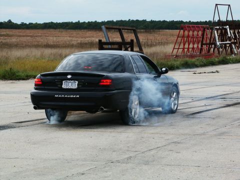 2001 Mercury Grand Marquis - A black sedan performs a burnout, kicking up a cloud of smoke from its rear tires on a paved surface.
